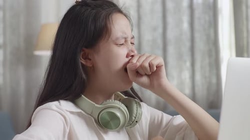 Bored Asian Teenager Yawning While Doing Home Work On Laptop , Student Learning Online At Home