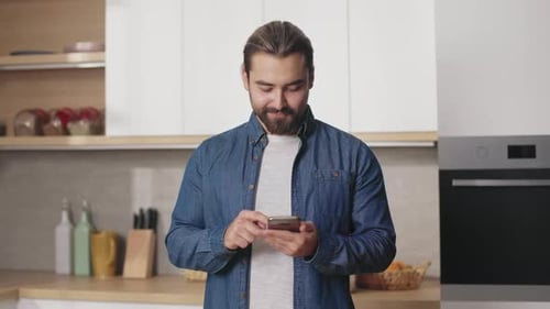 Smiling Man Using Smartphone in Modern Kitchen