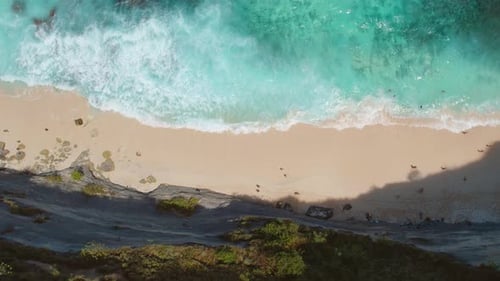 Stunning aerial view of a pristine beach with turquoise waters crashing against the shore, surrounde