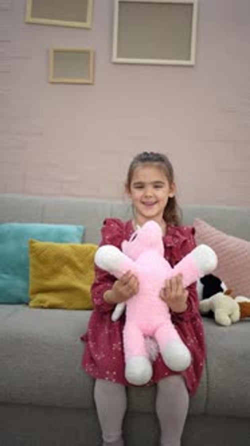 Little girl playing with her pink plush unicorn on the sofa