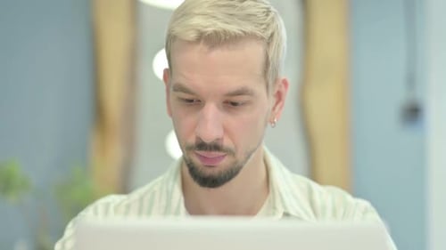 Close Up of Young Man Looking at Camera while using Laptop