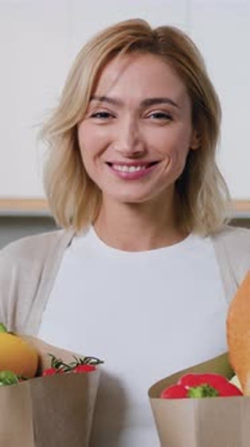 Smiling Woman Holding Fresh Groceries in Brown Paper Bags