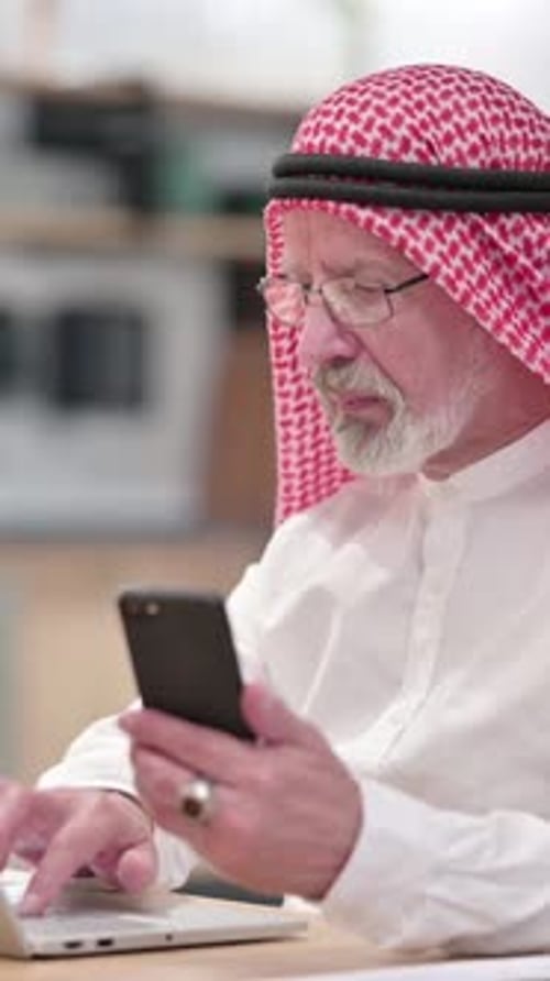 Man in Traditional Dress Uses Phone and Laptop