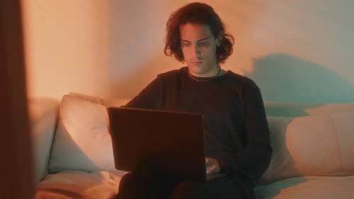 Young Adult Uses Laptop While Relaxing at Home