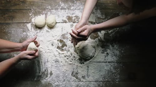Three People Kneading Dough on Wooden Surface