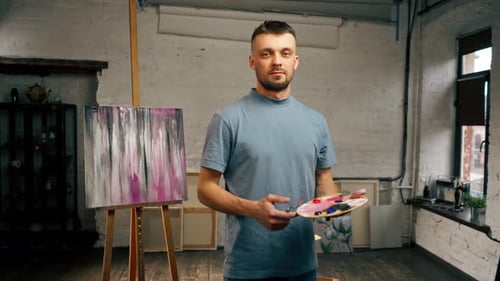 in an Art Studio an Artist Stands Directly at the Camera with Palette and Smiles