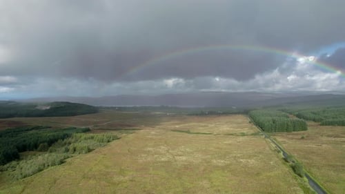 High aerial drone footage in the rain rolling right above a long, straight road looking towards a bi