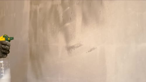 Hand Dampens White Painted Wall with Spray Bottle