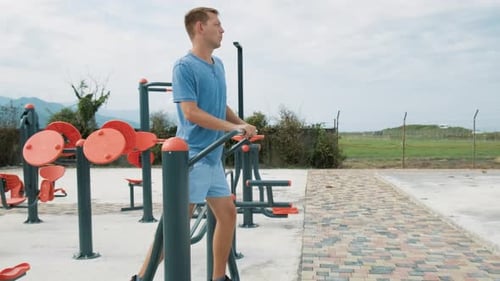 Cheerful Man Doing Cardio Workout Exercises on Elliptical Trainer in a Street Gym and Smiling Active