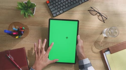 Top down view of man's hands using a mock up green screen tablet on a desk