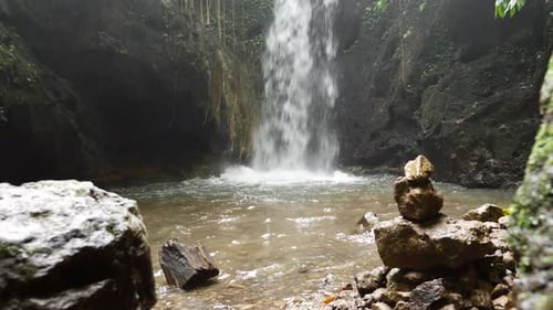A dolly shot of a pool of water, created by a small waterfall, surrounded by rocks and cliffs in the