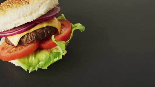Video of cheeseburger with salad in burger bun, on grey background with copy space