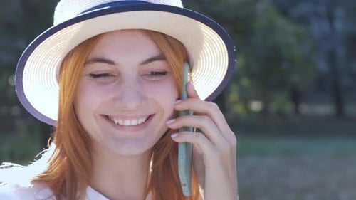 Pretty Teenage Girl with Red Hair Speaking on Mobile Phone Outdoors