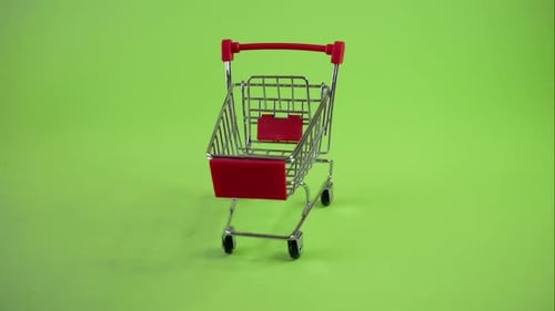 empty supermarket cart with red details stands on green background,