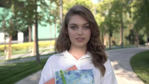 Smiling Woman Holding Notebooks Outdoors in Urban Park