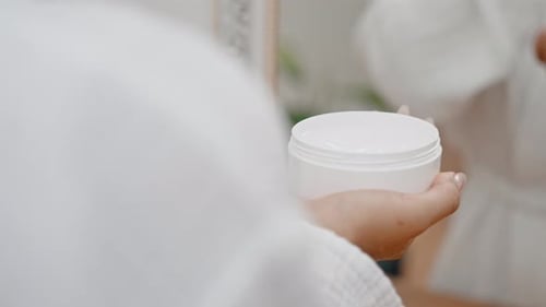 Woman Holding Cream Jar in Bathroom Mirror