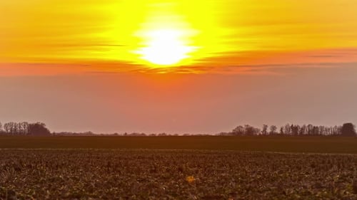 Static shot of brown agricultural field with sun setting in the background on a cloudy day in timela