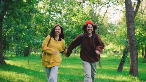 A Happy Couple Runs Hand in Hand Through a Park Surrounded By Trees Their Smiles Reflecting Joy and