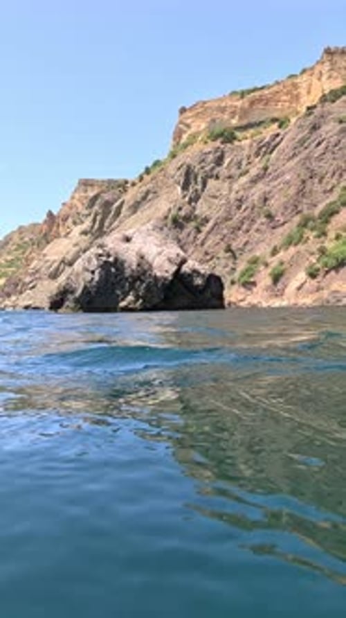 Sea Water Surface Camera Flies Over the Calm Azure Sea with Volcanic Rocky Shores on Background