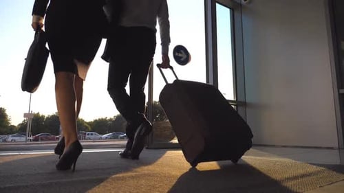 Empresários saindo do aeroporto pela porta de vidro automática com sua bagagem, rapaz e mulher