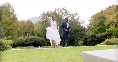 Happy african american bride and groom jumping and embracing at their wedding in garden, slow motion