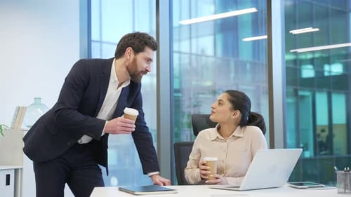 Businessman treats female coworker to coffee at workplace in business office. Two colleagues engaged