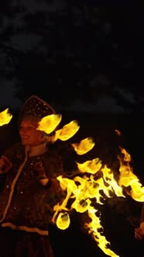 Spectacle de feu nocturne spectaculaire avec une danseuse costumée traditionnelle faisant tourner des ventilateurs flamboyants contre un