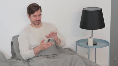 Man Using Smartphone While Sitting in Bed
