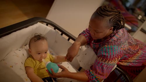 Woman Feeds Baby With Bottle in Crib
