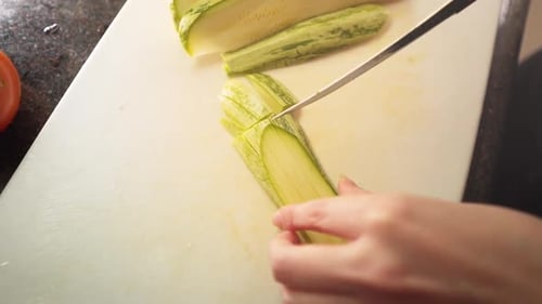Female hands cutting a green zucchini in the kitchen in slow motion