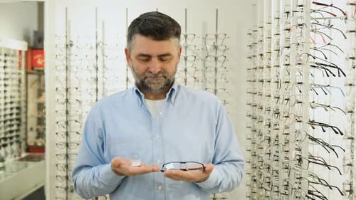 Hombre mayor sostiene lentes de contacto y anteojos en las manos