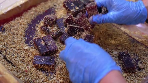 Las manos con guantes azules cubren pequeñas barras de mermelada con frutos secos.