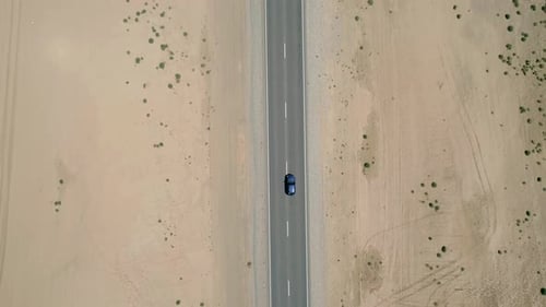 Aerial Top Down View of a Car Driving on a Highway Road Between Sands with Little Green Grass Bushes