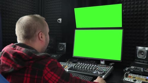 Toningenieur am Arbeitsplatz mit Greenscreen-Monitoren, Rückansicht eines Mannes beim Audiomischen