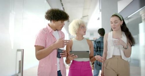 Collaborating on project details, colleagues using tablet in modern office hallway
