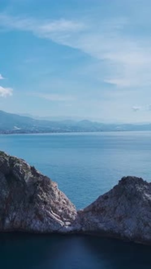 Vertical Video of a Massive Rock Standing in the Open Ocean With Waves Gently Washing Against Its