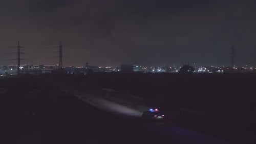 Night aerial footage of a police car driving down a dark urban area