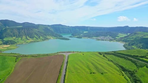 Lush green hills surrounding a tranquil lake on a clear day, aerial view