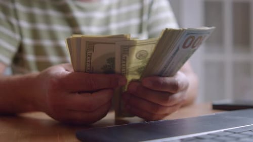Caucasian Freelancer Counting Dollar Bills At Home Office Desk With Laptop