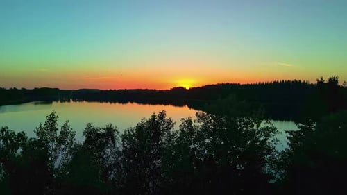 Beautiful Sunset Over a Calm Lake with Silhouette of Trees from an Aerial Drone Dolly Shot.