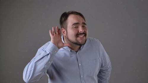 Mann im blauen Hemd gestikuliert mit Hand an Ohr, um zuzuhören