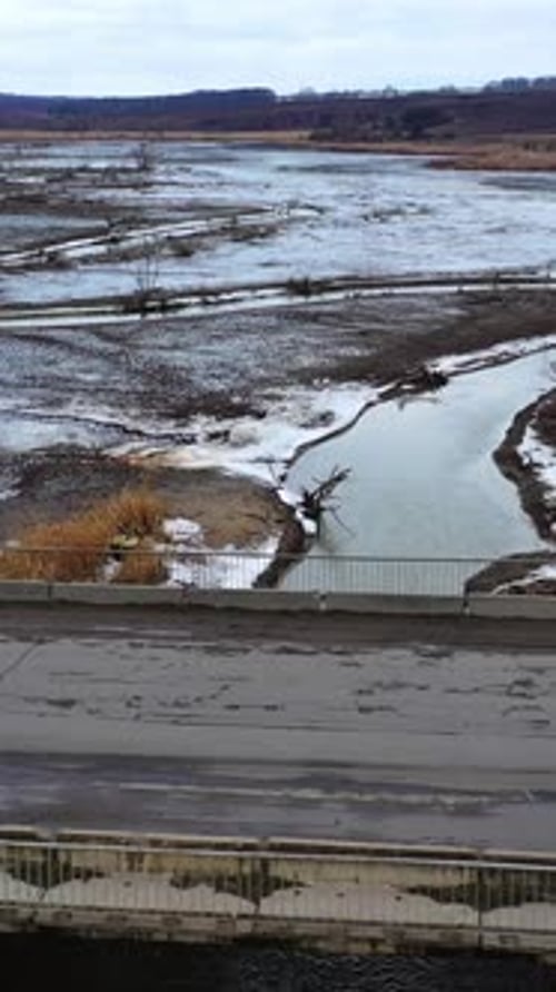 Gloomy scene of nature. Polluted river floating under the bridge on muddy background in springtime.