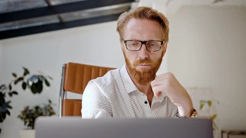 Thoughtful Man Working at Laptop in Office