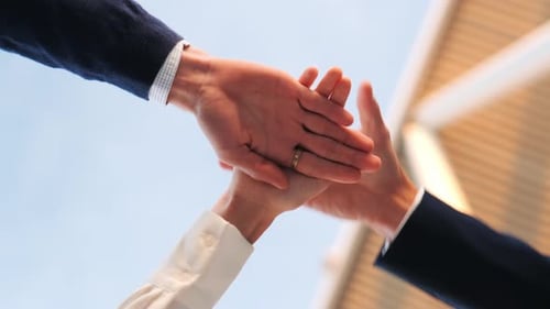 Three hands from different directions stack in unity under the sky, demonstrating teamwork