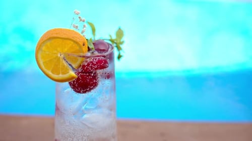 Mojito cocktail glass with ice and cherry and mint, soda and gin near a blue pool close up