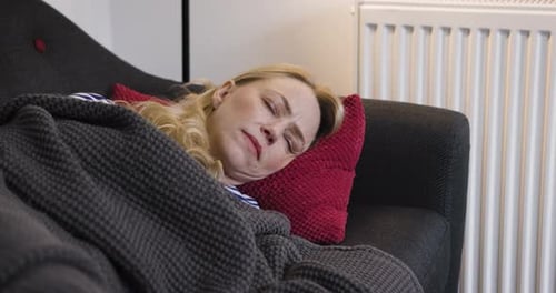 Woman Lays on Couch Under Blanket