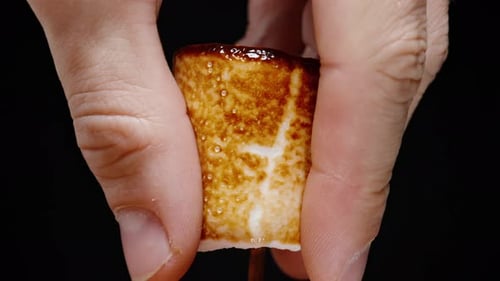 Fingers Compressing a Toasted Marshmallow on a Stick