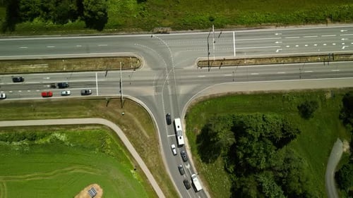 Uma vista aérea captura a agitação de um cruzamento rural com vários veículos e uma vegetação exuberante
