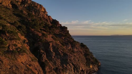Drone footage of a sunset-lit, jagged-looking, seaside cliff along the coast of the Mediterranean Se