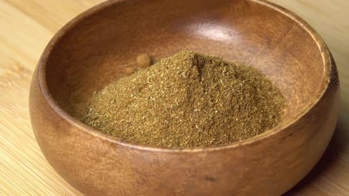 La
especia de lúpulo Khmeli suneli se encuentra en un cuenco de madera y gira sobre una tabla de madera. Condimento seco en cuchara